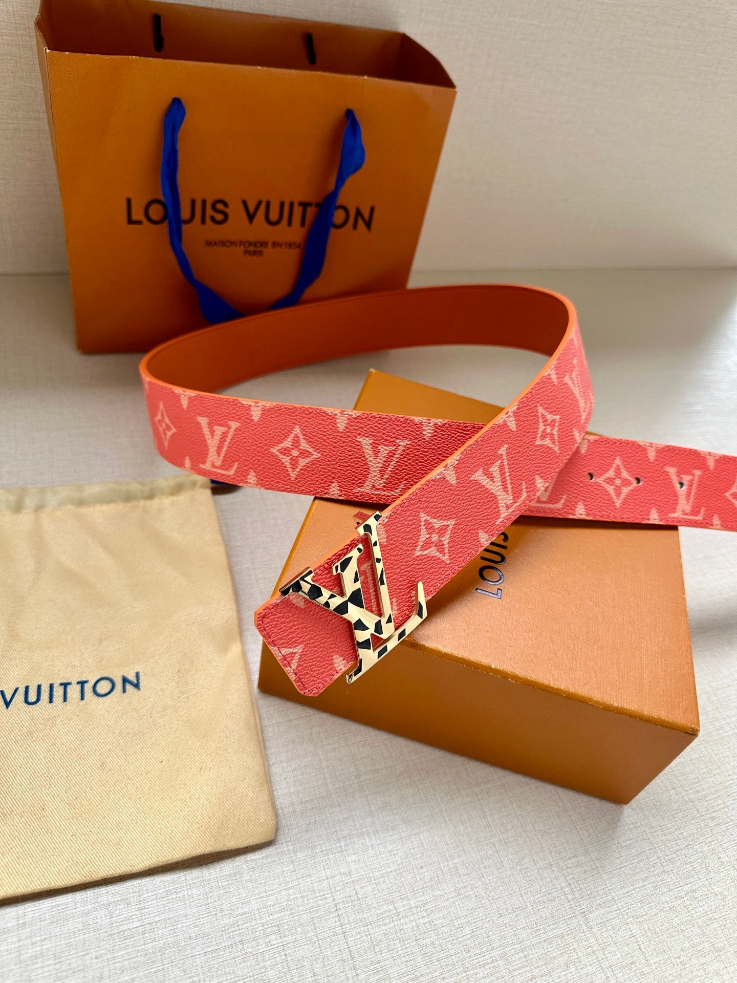 Red monogram belt with metal buckle and foldover keeper, straps overlapping.