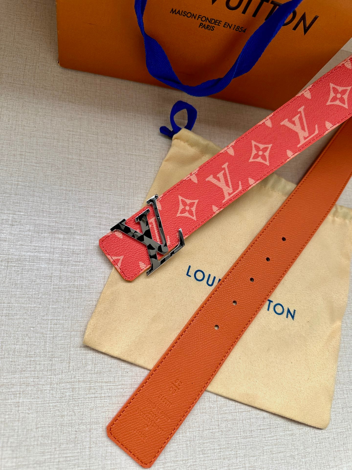 Red monogram belt with metal buckle and orange leather keeper strap with holes.