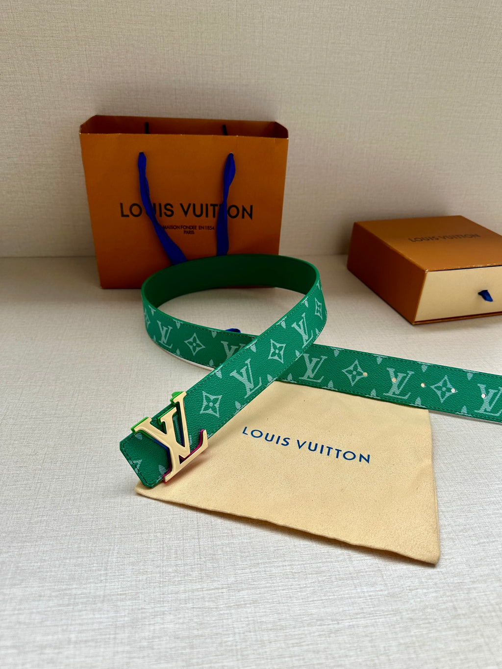 Green Louis Vuitton belt with white monogram and gold-tone LV buckle, laid across bag