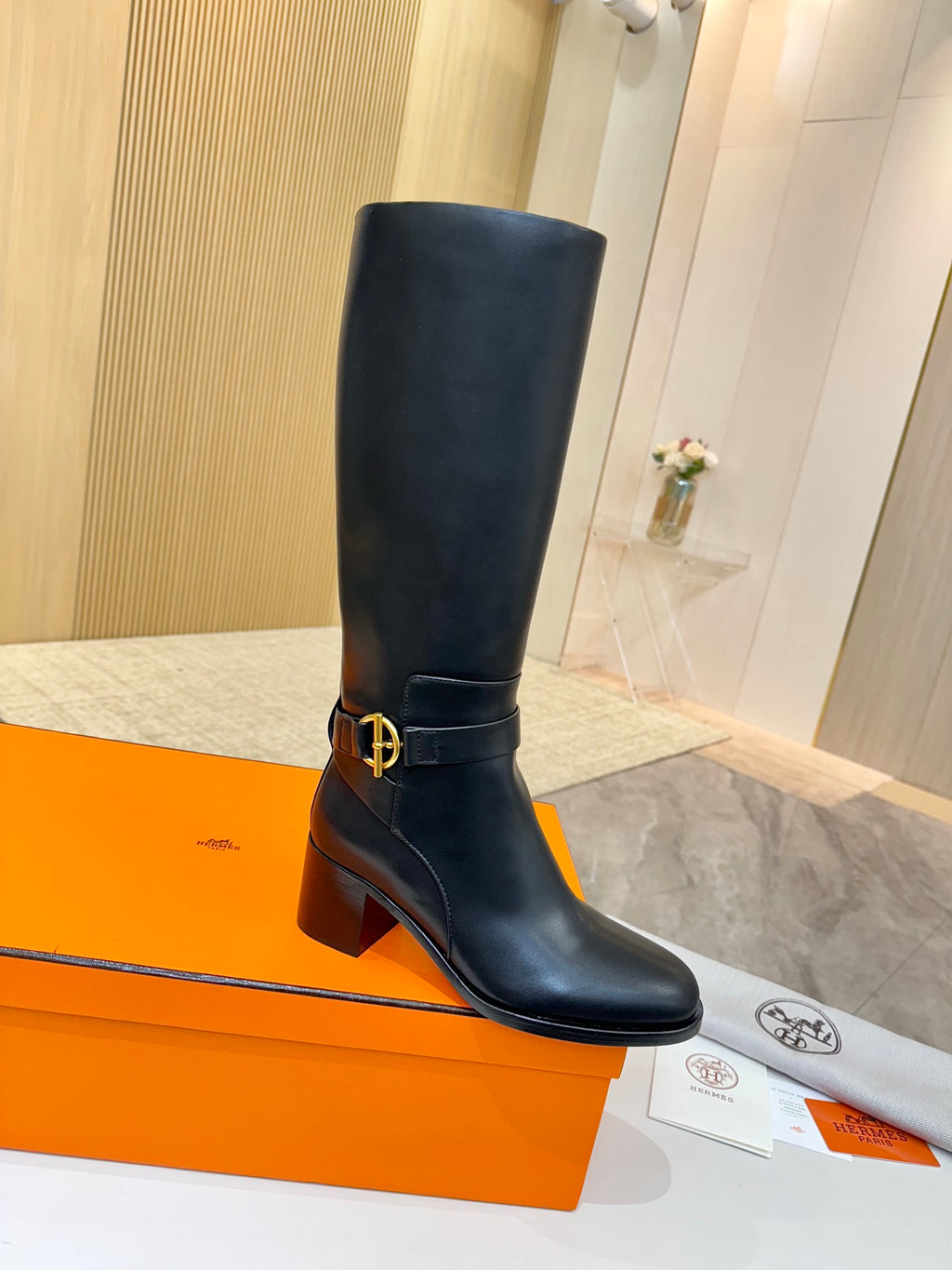 Black leather knee-high boots with gold logo buckle and chunky heel