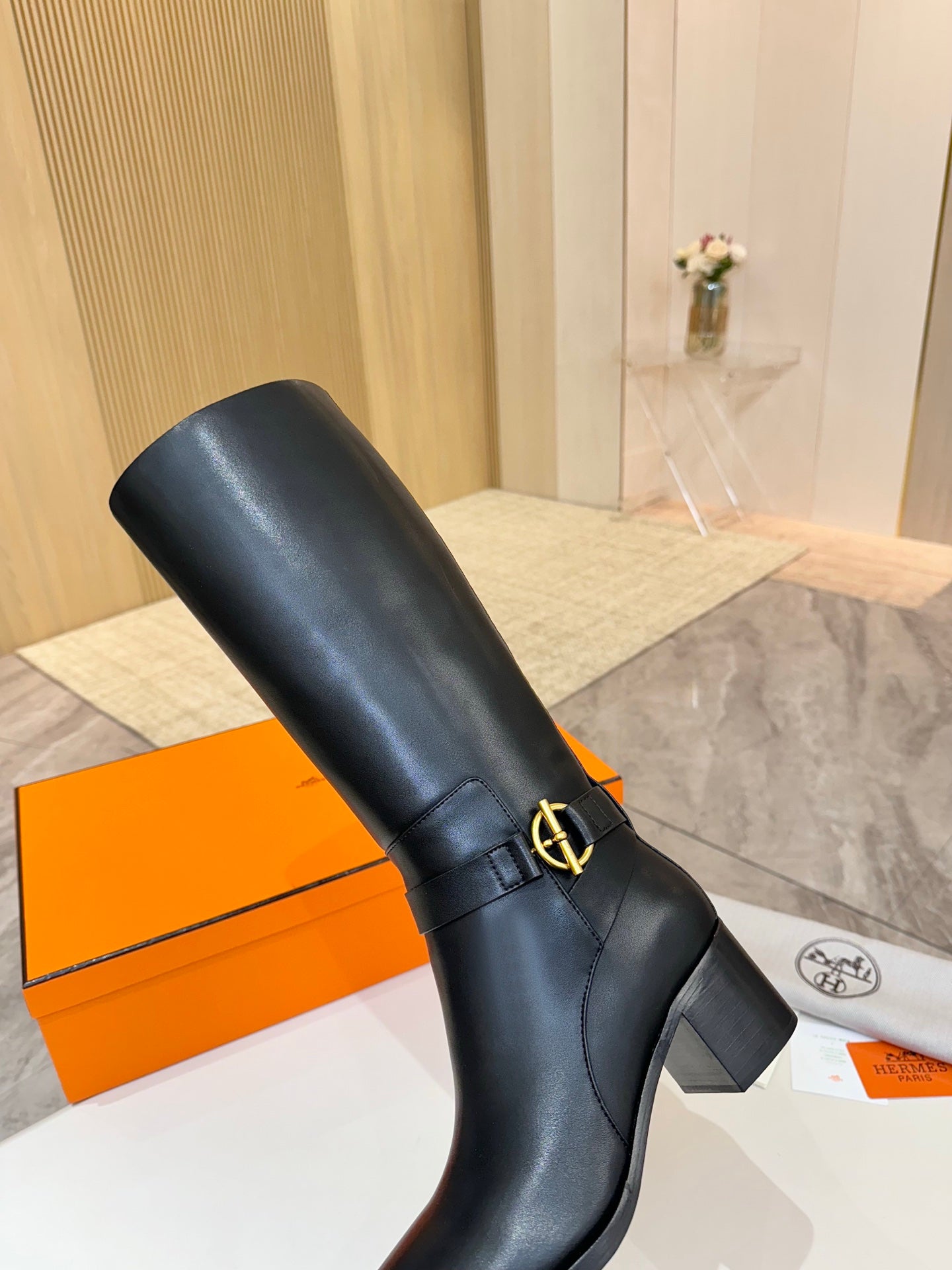 Black leather knee-high boot with gold logo buckle and mid-height heel