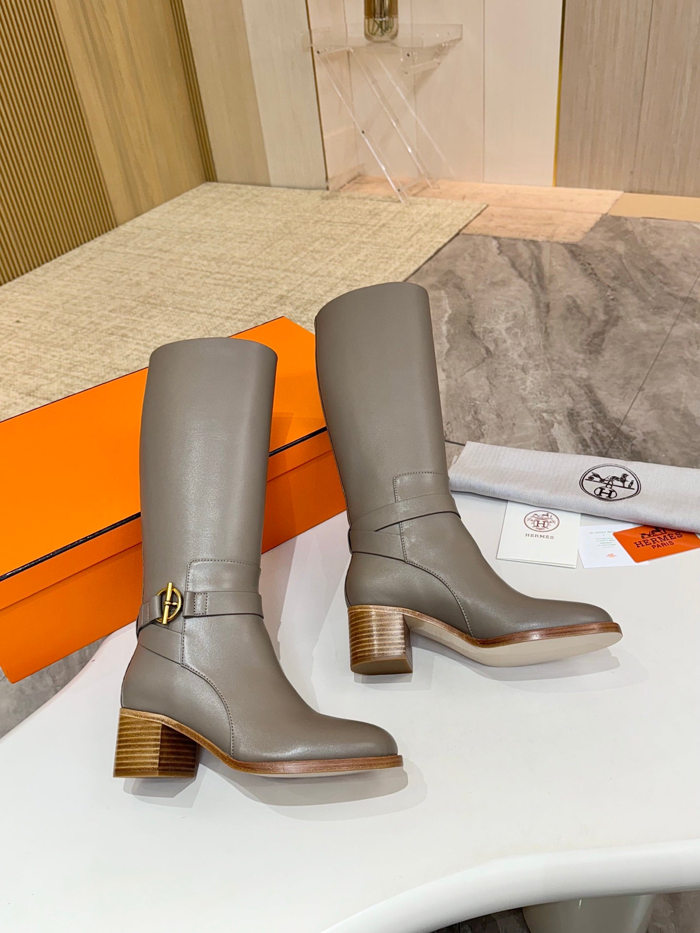 Pair of women’s gray knee-high heeled boots with gold-tone ankle buckle and stacked heel
