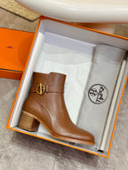Brown leather ankle boots in open orange box, with gold buckle strap