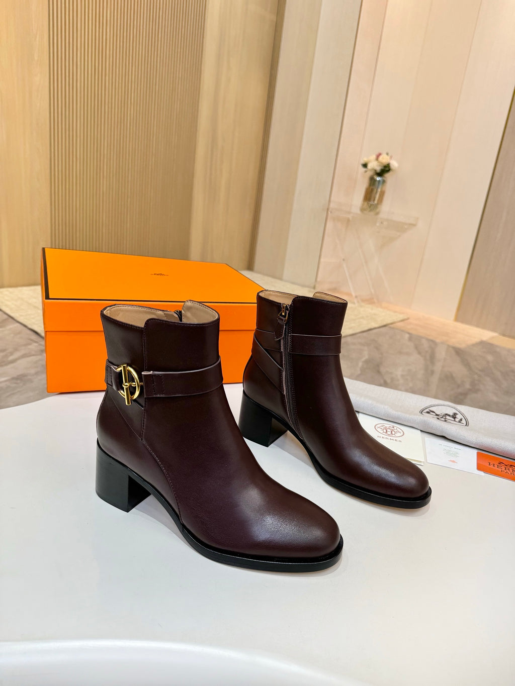 Brown leather heeled ankle boots with gold logo buckle, front angle
