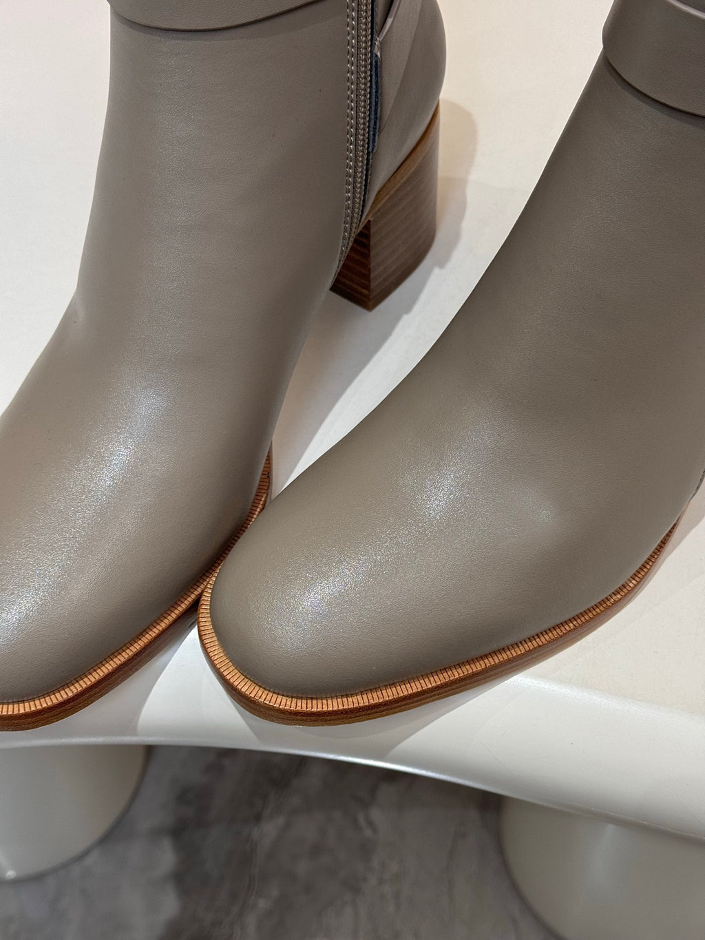Close-up of light gray ankle boot leather with side zipper and stacked heel