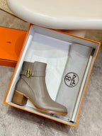 Light gray ankle boot with side gold buckle and dust bag in orange box