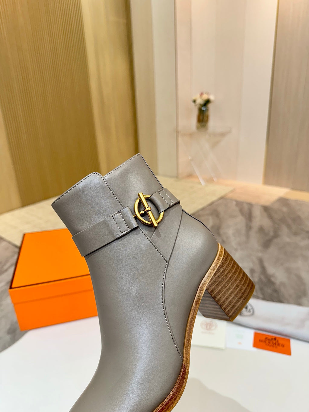 Light gray leather ankle boot with gold buckle strap and wooden heel