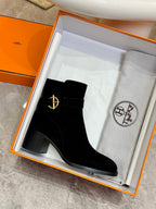 Black suede ankle boot with gold logo emblem, in an open orange box
