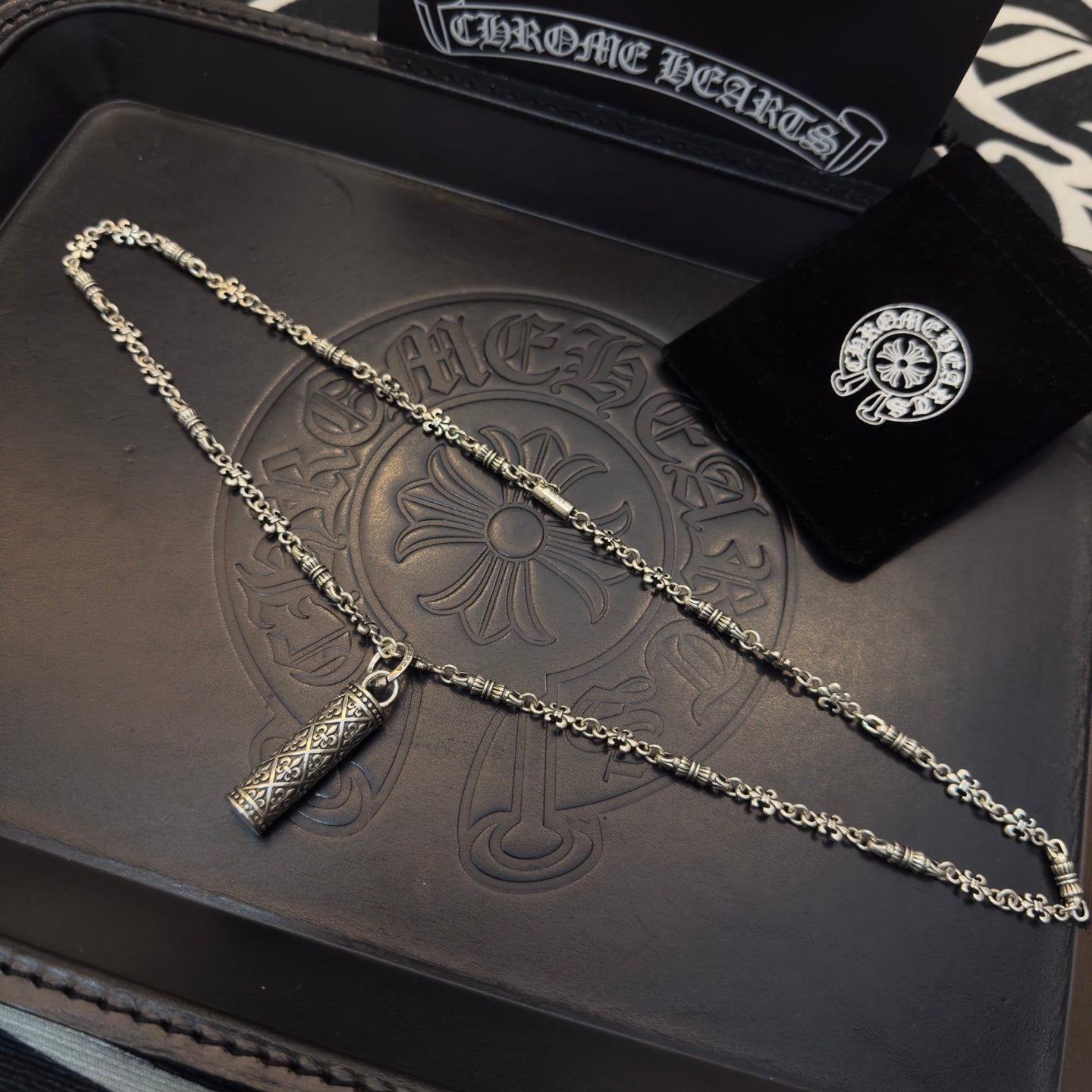 Gold-tone chain necklace with cylindrical pendant on embossed leather-style box