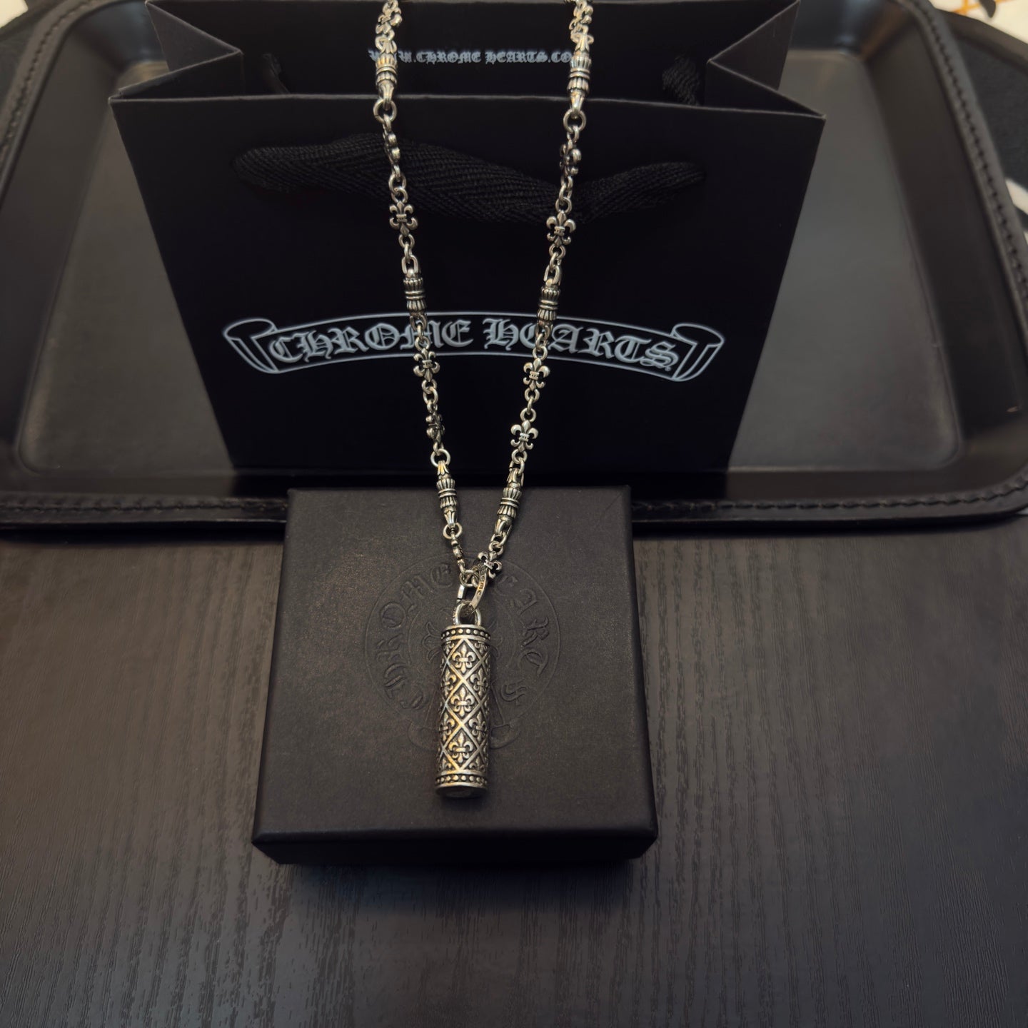 Gold-tone chain necklace with cylindrical engraved pendant on gift box
