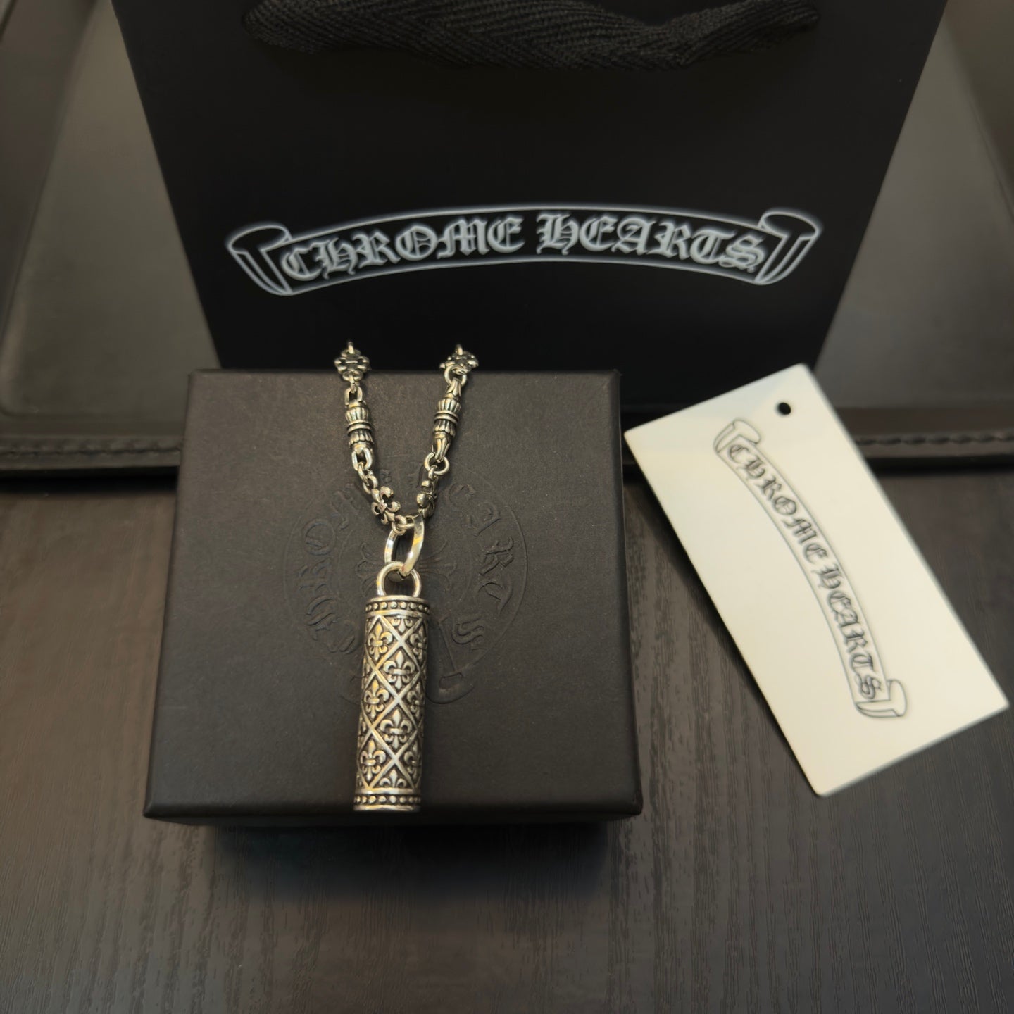 Gold-tone chain necklace with cylindrical engraved pendant on display box and tag
