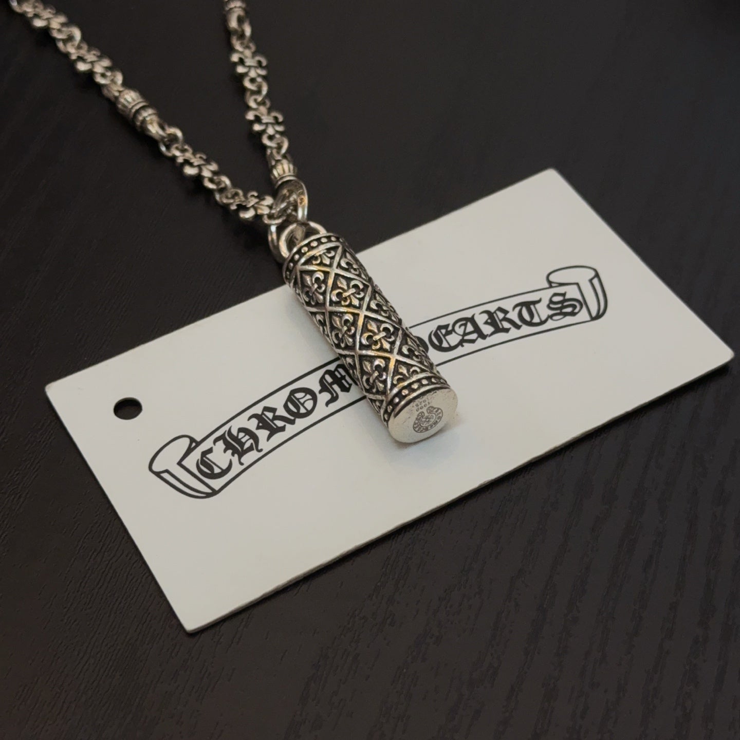 Gold-tone cylindrical pendant necklace with engraved detailing on hanging tag