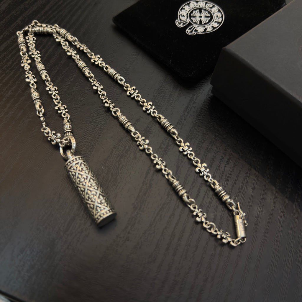Gold-tone chain necklaces with cylindrical engraved pendants on black box