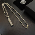 Gold-tone chain necklaces with cylindrical engraved pendants on black box