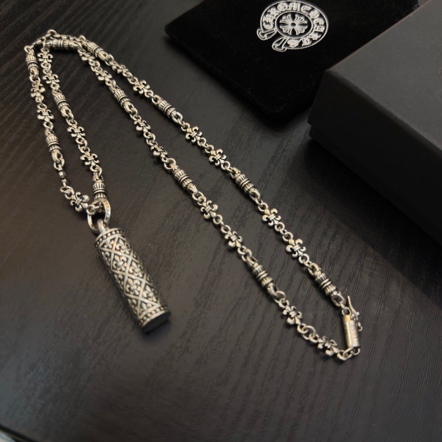 Gold-tone chain necklaces with cylindrical engraved pendants on black box