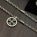 Close-up of silver-tone chain necklace with round pendant and teal stone accents.