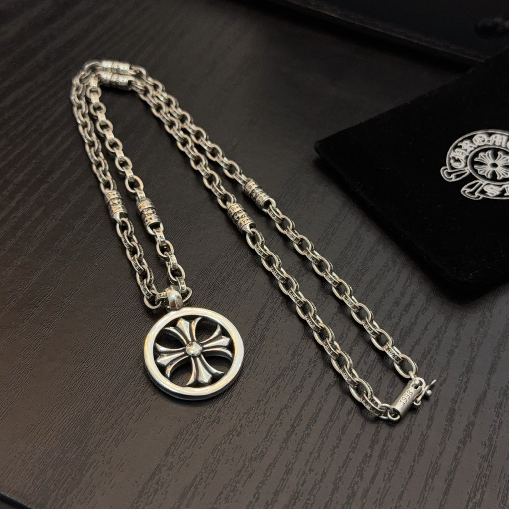 Silver-tone necklace with circular wheel pendant and teal stones, shown on box.