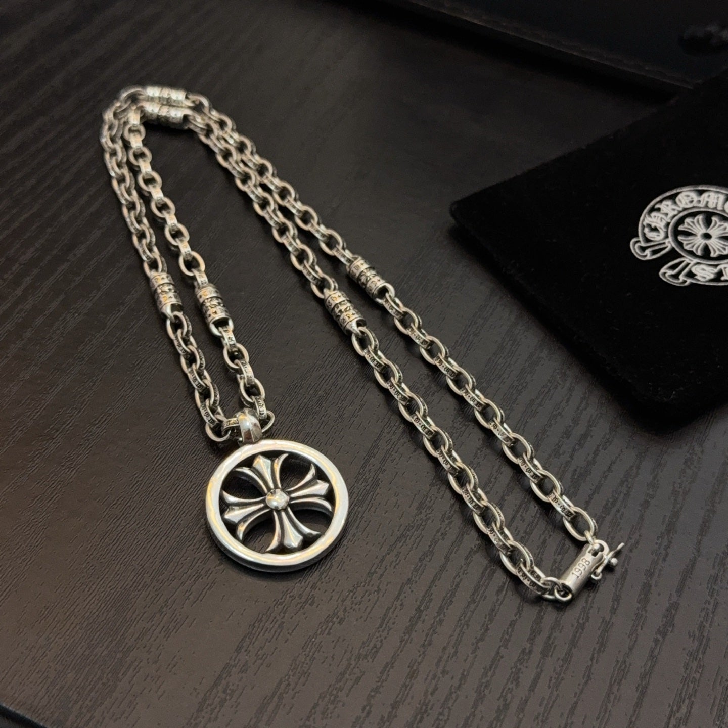 Silver-tone necklace with circular wheel pendant and teal stones, shown on box.