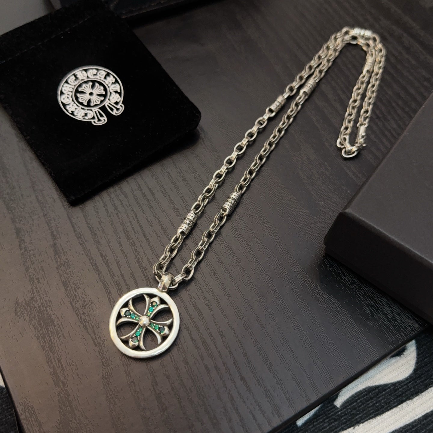 Silver-tone chain necklace with round pendant featuring teal stones, laid on display.