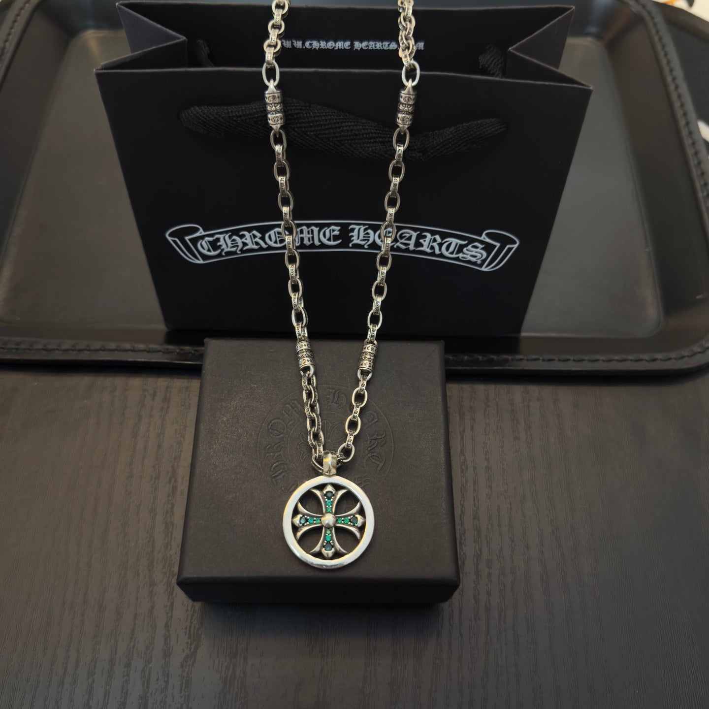 Silver-tone necklace with round pendant and teal insets, shown on gift box.