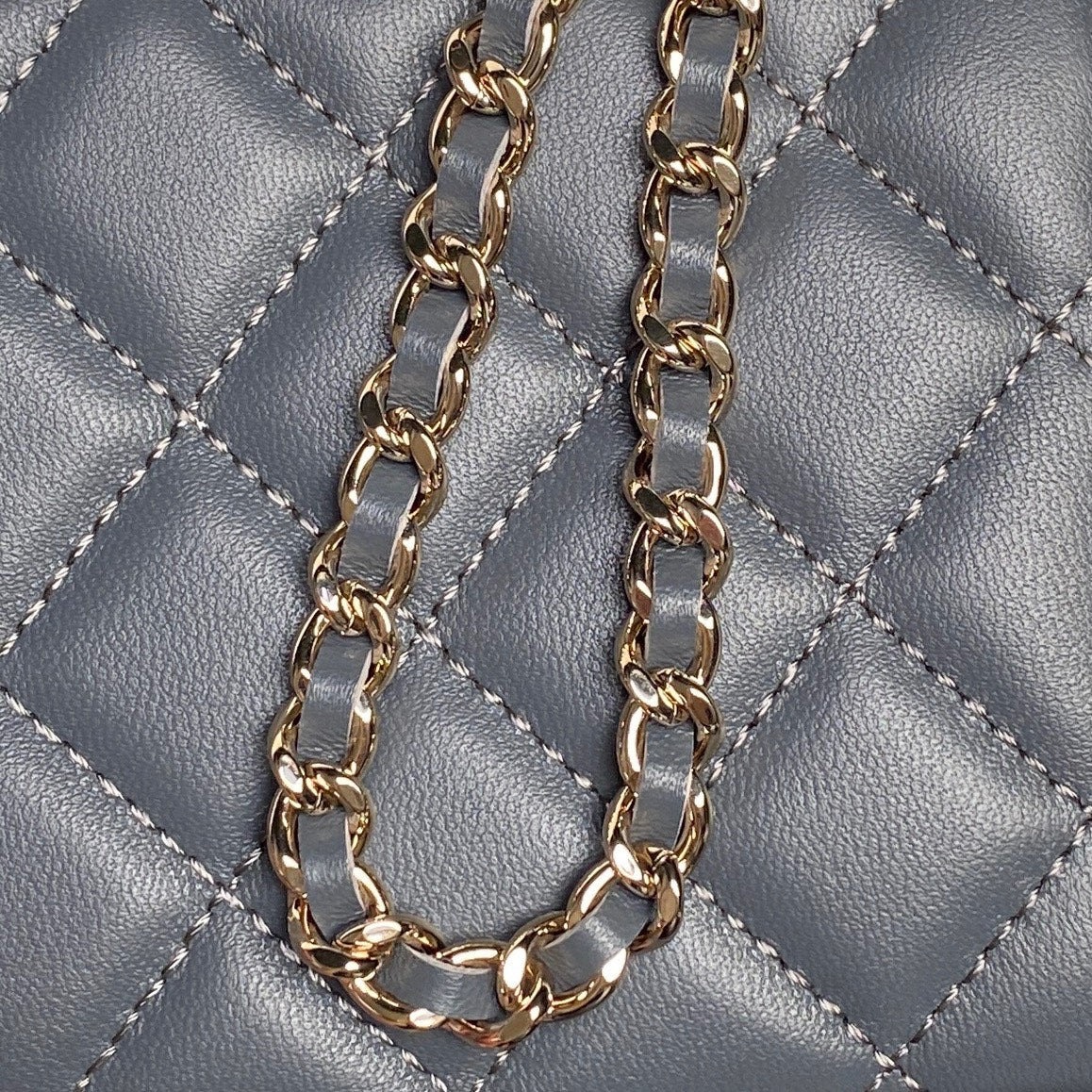 Gold chain strap detail on blue quilted mini handbag with metal links