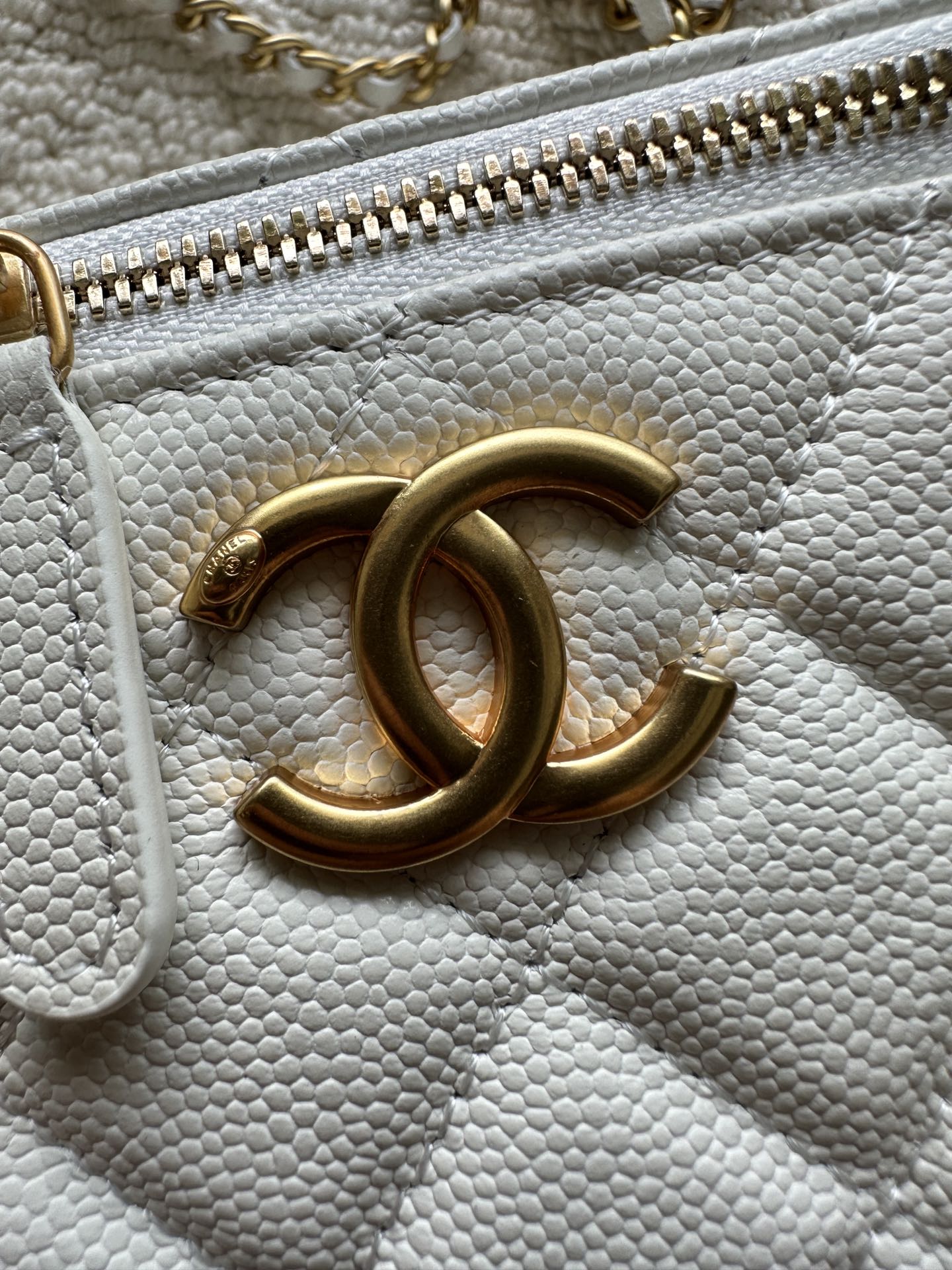 Chanel quilted mini bag close-up of gold zipper and CC logo on white leather