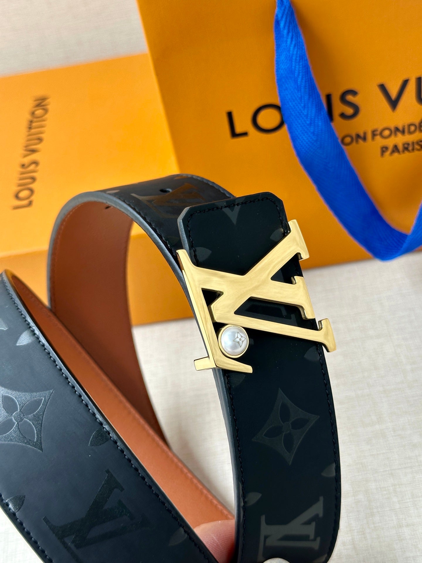 Louis Vuitton belt close-up: dark monogram strap with gold LV buckle and gem
