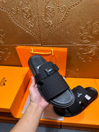Hand-holding black textured slide sandal with H buckle strap