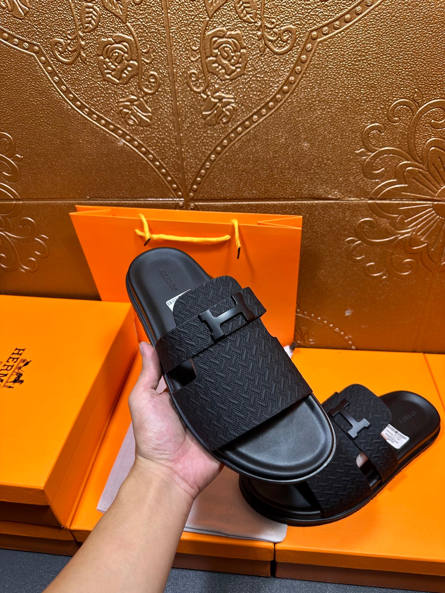 Hand-holding black textured slide sandal with H buckle strap