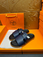 Hermes dark blue slide sandals with wide buckle straps, shown on box