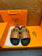 Hermes leather slide sandals with tan straps, black H buckle, and black footbed
