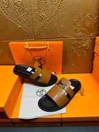 Hermes slide sandals with tan leather crossover straps and black H buckle on dark sole