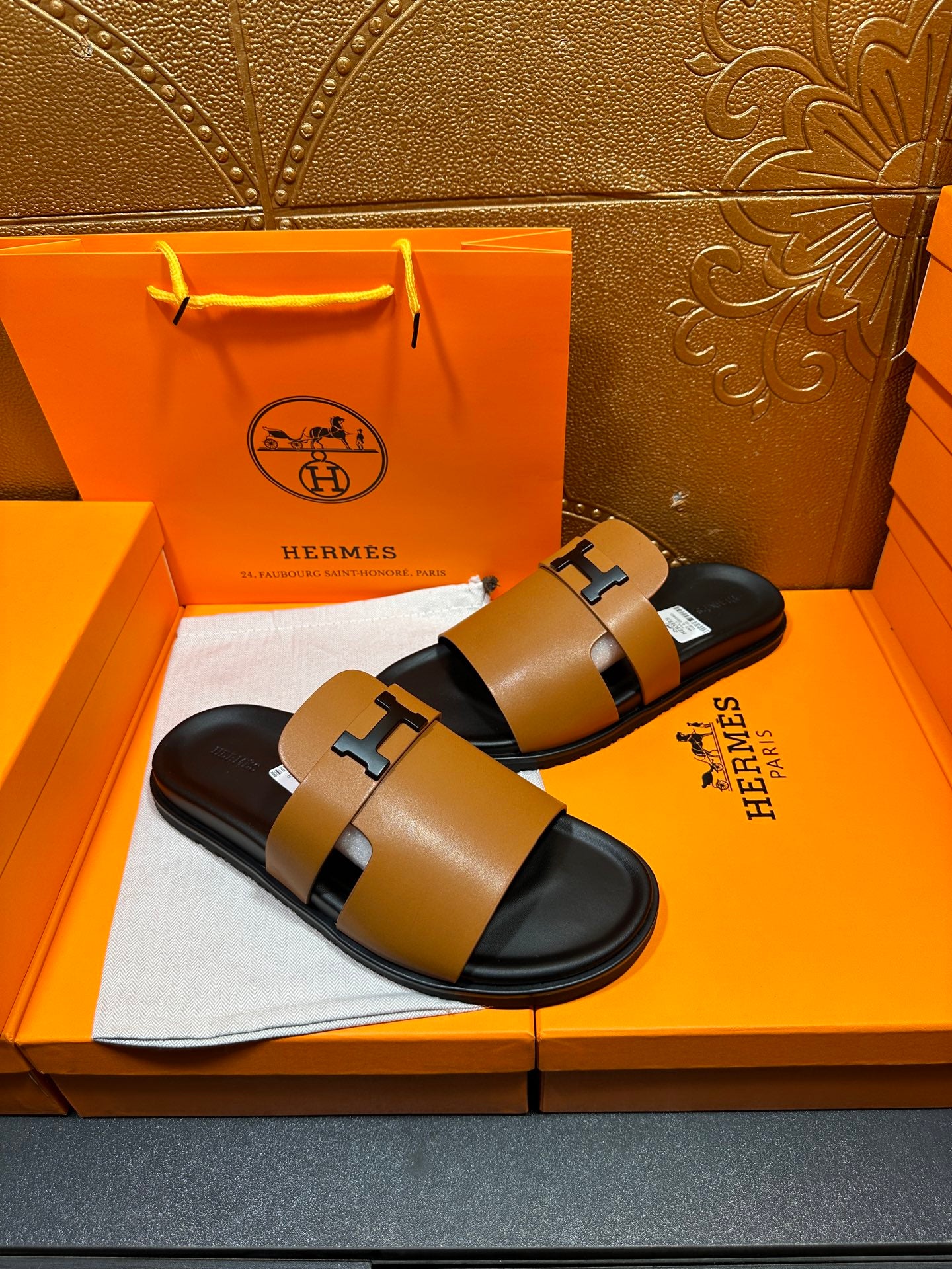 Hermes slide sandals with wide tan straps, black H buckle, and cushioned black footbed