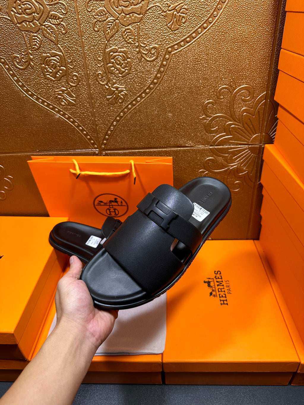 Black leather slide sandals held by hand, wide straps and adjustable buckle, cushioned footbed