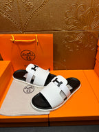 Hermes slide sandals with white straps, black soles, shown on display