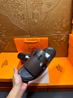 Dark leather slide sandals held in hand, wide strap with buckle detail.