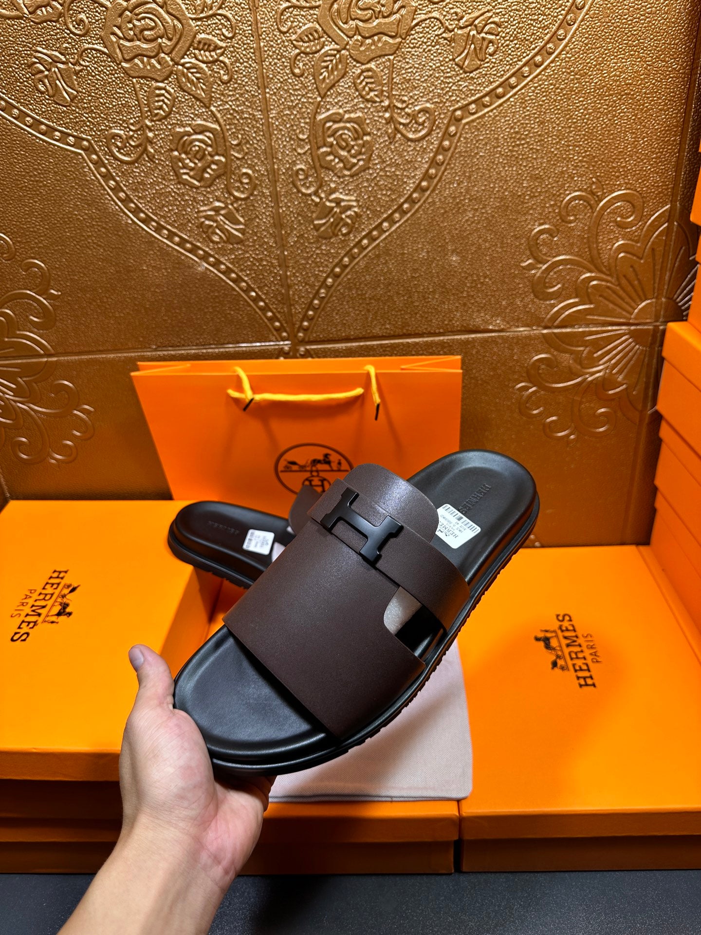 Dark leather slide sandals held in hand, wide strap with buckle detail.