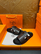 Dark leather slide sandal with wide front strap and buckle, open toe.