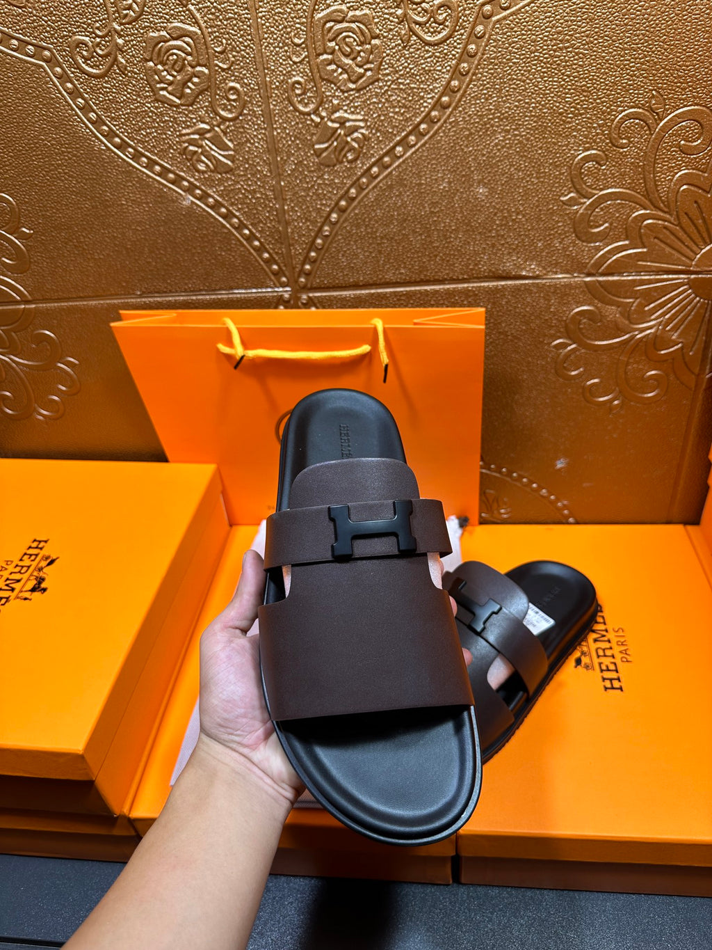 Dark leather slide sandal held up, single front buckle strap, open toe.
