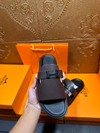 Dark leather slide sandal held up, single front buckle strap, open toe.