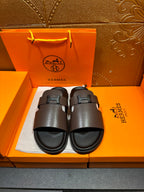 Dark leather slide sandals with adjustable buckle strap, open toe.