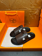 Dark leather slide sandals with wide strap and buckle detail, open toe.