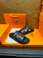 Pair of dark leather slide sandals with wide buckle strap, open toe.