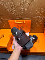 Dark leather slide sandal held in hand, wide buckle strap and open toe.