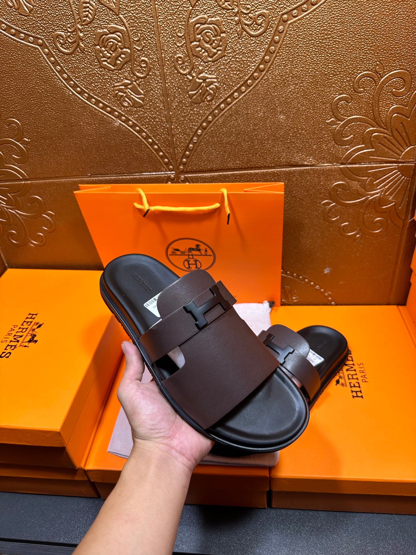 Dark leather slide sandal held in hand, wide buckle strap and open toe.