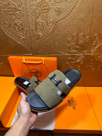 Hand holding olive suede slide sandals with H buckle straps and black footbed