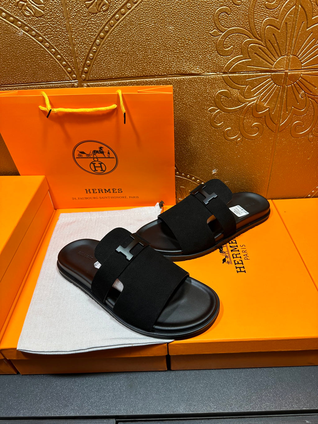 Hermes black slide sandals with wide strap and H logo buckle, angled view