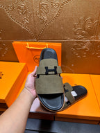 Hand holding olive suede slide sandals showing front H buckle strap