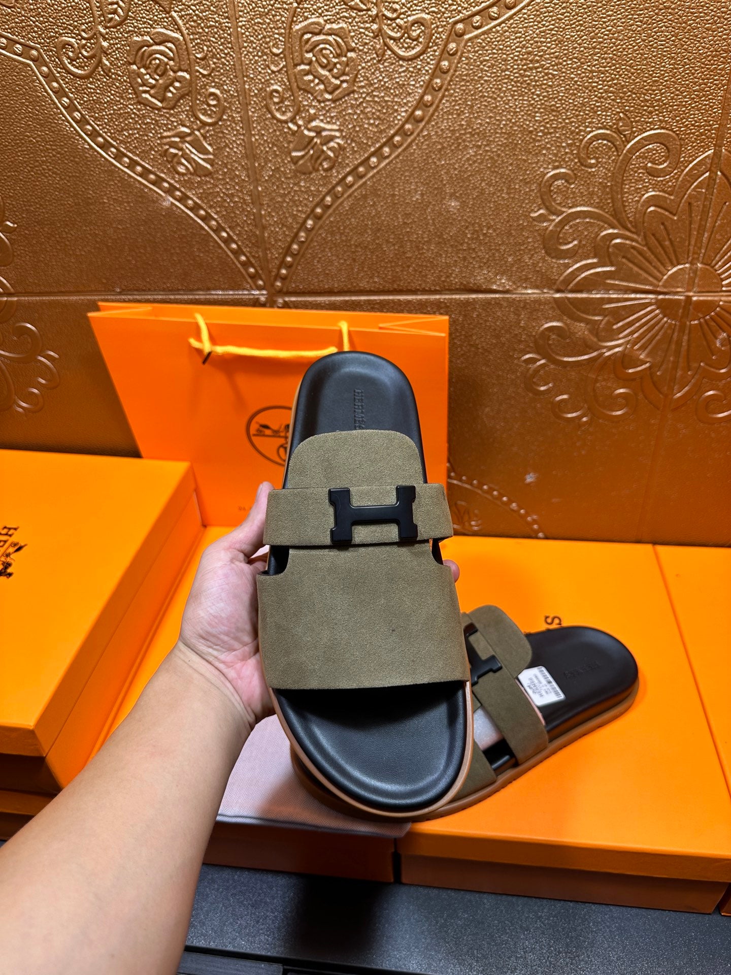 Hand holding olive suede slide sandals showing front H buckle strap