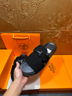 Hermes black slide sandals held in hand, H buckle straps visible